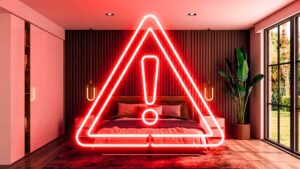 Imagem conceitual de um quarto luxuoso e moderno onde, flutuando sobre uma cama perfeitamente arrumada com roupa de cama 100 algodão branca e travesseiros macios, há um grande ícone de alerta de perigo (triângulo com exclamação) em neon vermelho brilhante. O brilho do neon reflete sutilmente sobre a roupa de cama branca.